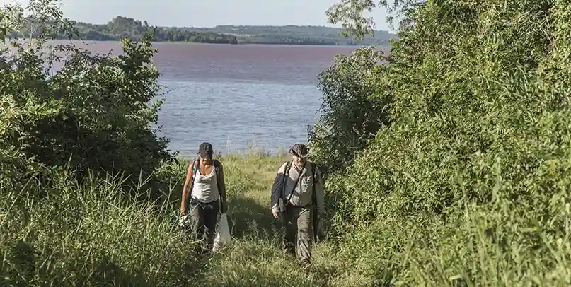 Dos personas caminando por el predio del Barrio Cerrado La Selva en Candelaria, Misiones, con el río Paraná de fondo entre la vegetación nativa