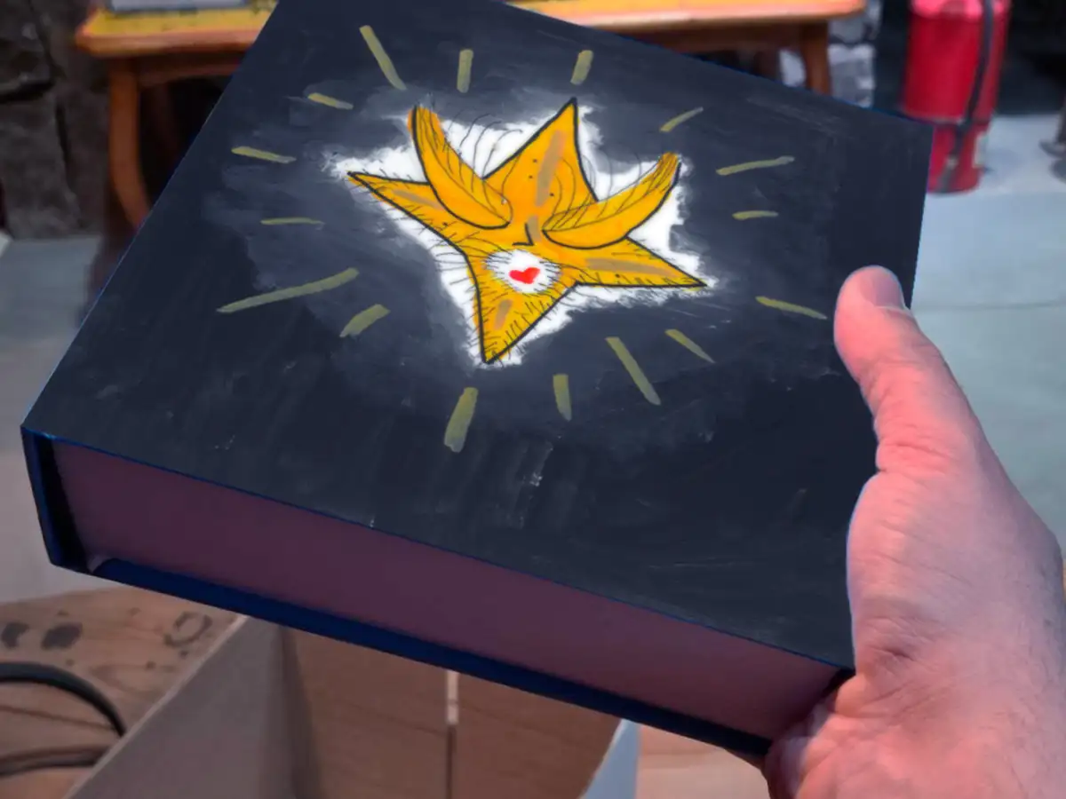 Mano que sostiene el libro El Portal de la Navidad. En la tapa oscura se ve una estrella amarilla con un corazón rojo, rodeada de rayos de luz.